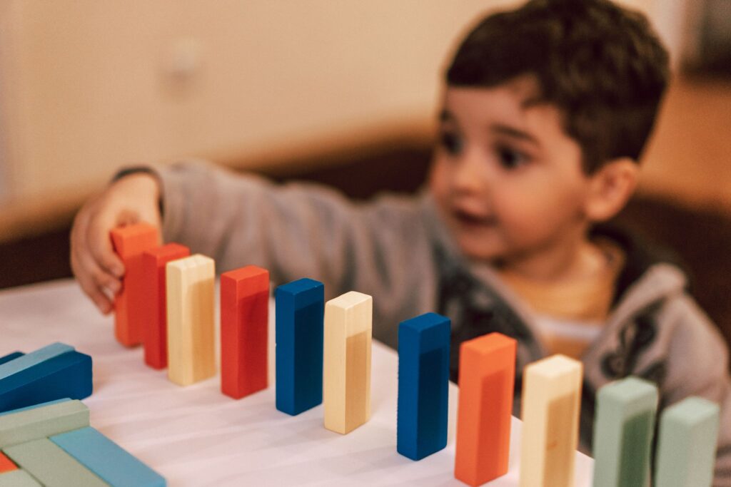 A young boy plays with colorful wooden blocks indoors, focusing intently and learning through play.
